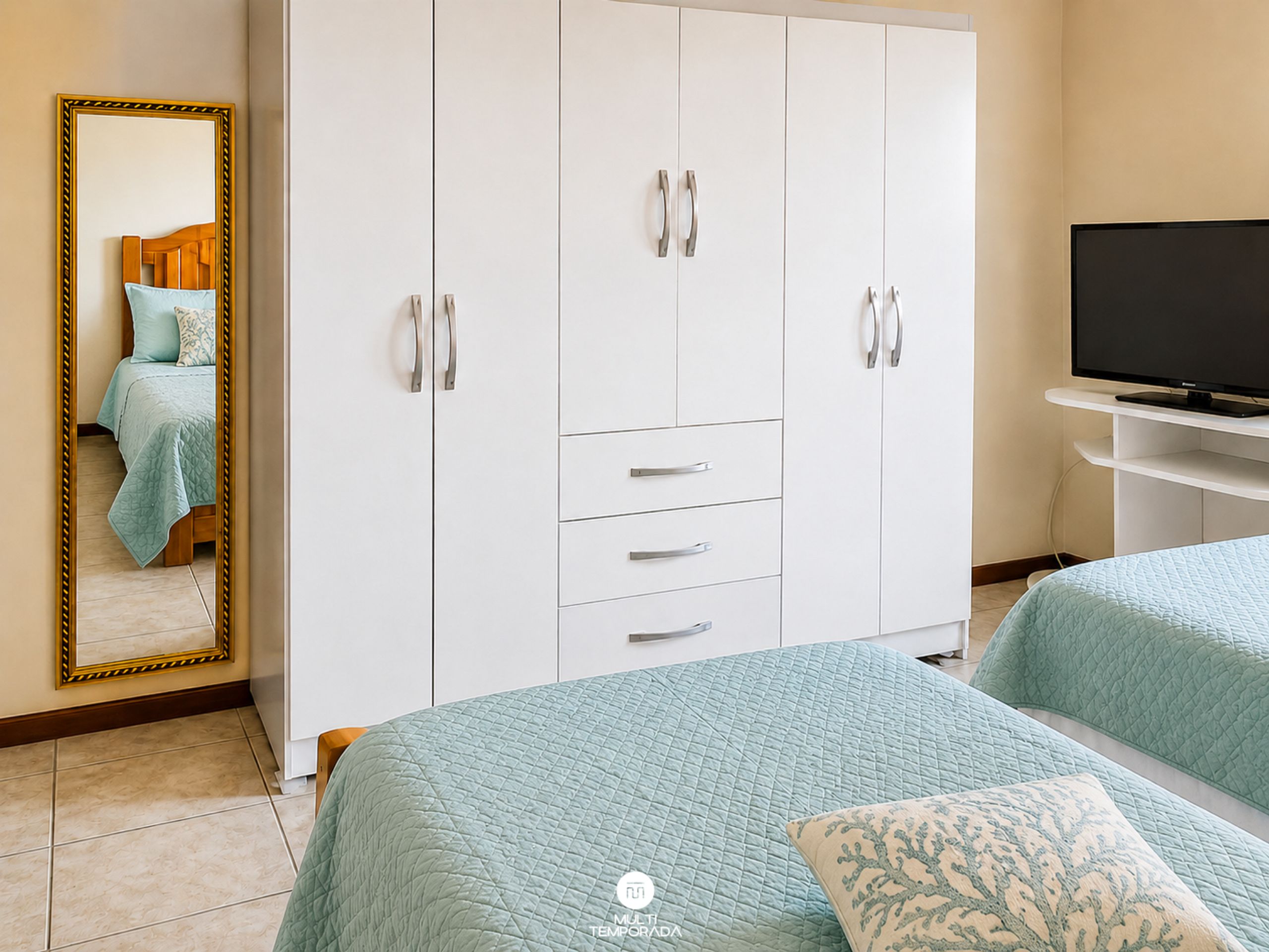 A bedroom with a bed, a wardrobe, a television, and a mirror.