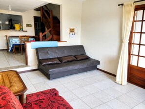 Ein Wohnzimmer mit einer Couch, einem Esstisch mit Stühlen und einer Treppe, die in eine obere Ebene führt.