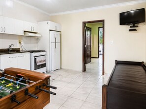 A kitchen with white cabinets, a stove, a refrigerator, and a foosball table. - Casa Estrela Cond Fechado c Piscina - RJ (Cabo Frio)