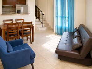 A living room with a sofa, chairs, a dining table, and a kitchen area with appliances. - Casa Estrela Cond Fechado c Piscina - RJ (Cabo Frio)