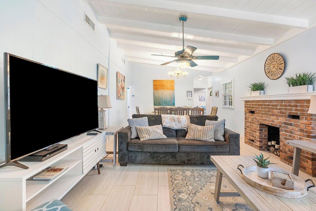 A modern living room with a flat-screen TV, a sofa, a fireplace, and a ceiling fan.