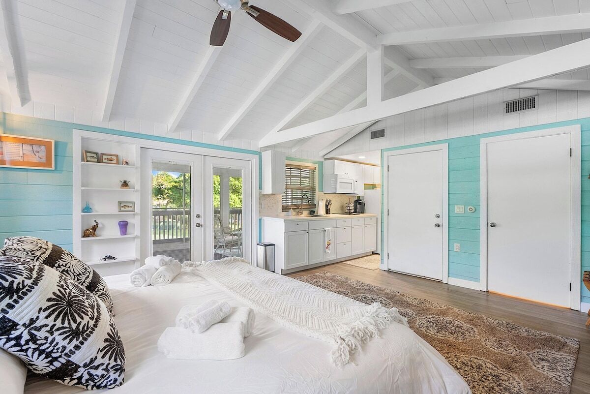 A bedroom with a bed, a ceiling fan, a bathroom with a shower, and a kitchen area.