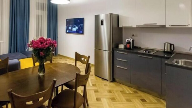 A modern kitchen with a refrigerator, stove, and sink. There is a dining table with chairs and a vase of flowers. - Luxury 3BR Apartment by Freedom Squre Tbilisi Georgia (T'bilisi)