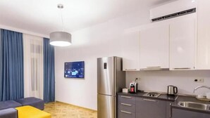 A modern kitchen with a refrigerator, stove, and sink. There is a wooden floor and a blue curtain. - Luxury 3BR Apartment by Freedom Squre Tbilisi Georgia (T'bilisi)