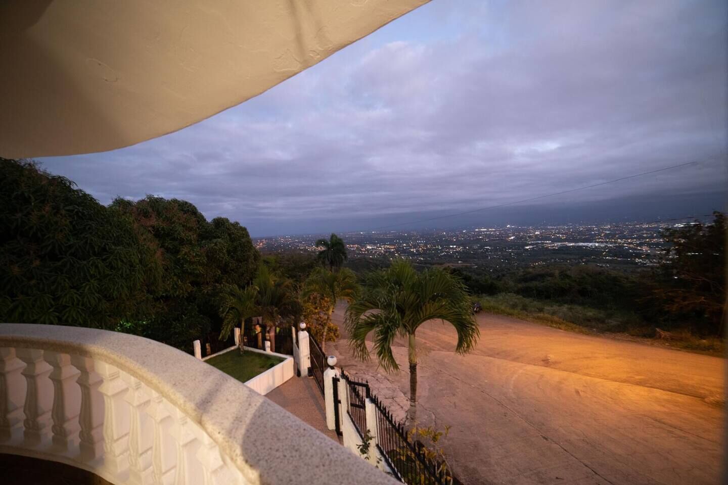 Un balcon offrant une vue sur le paysage urbain au crépuscule, avec des palmiers et une zone dallée.