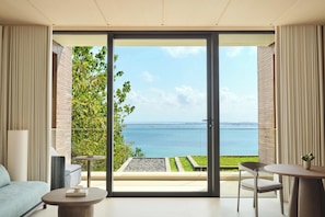 A modern room with a sliding glass door leading to a balcony overlooking a body of water and greenery.