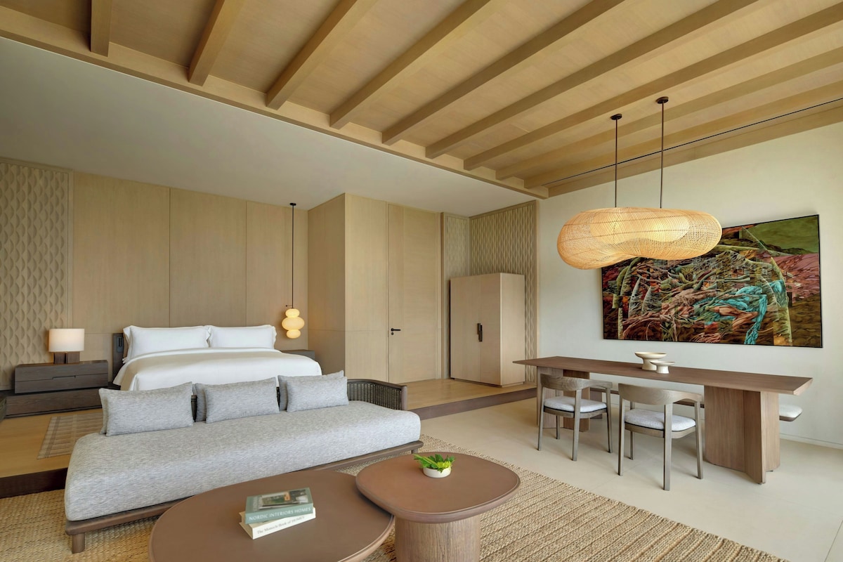 A modern hotel room with a bed, sofa, desk, and chairs.