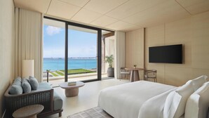 A modern hotel room with a large bed, a flat-screen TV, a seating area with a view of the sea, and a balcony.