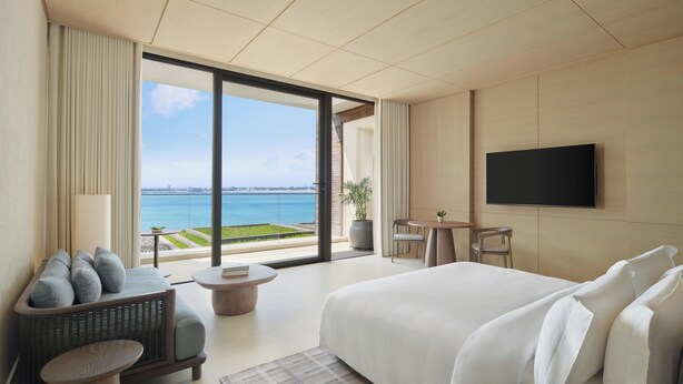 Ein modernes Hotelzimmer mit einem großen Bett, einem Flachbildfernseher, einer Sitzecke mit Meerblick und einem Balkon.