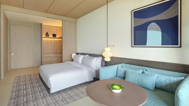 A hotel room with a bed, a sofa, a small table with a plant, and a painting on the wall.