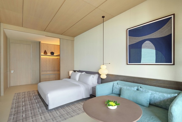 A hotel room with a bed, a sofa, a small table with a plant, and a painting on the wall.