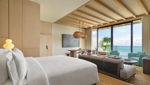 A modern hotel room with a large bed, a dining area, and a view of the ocean.