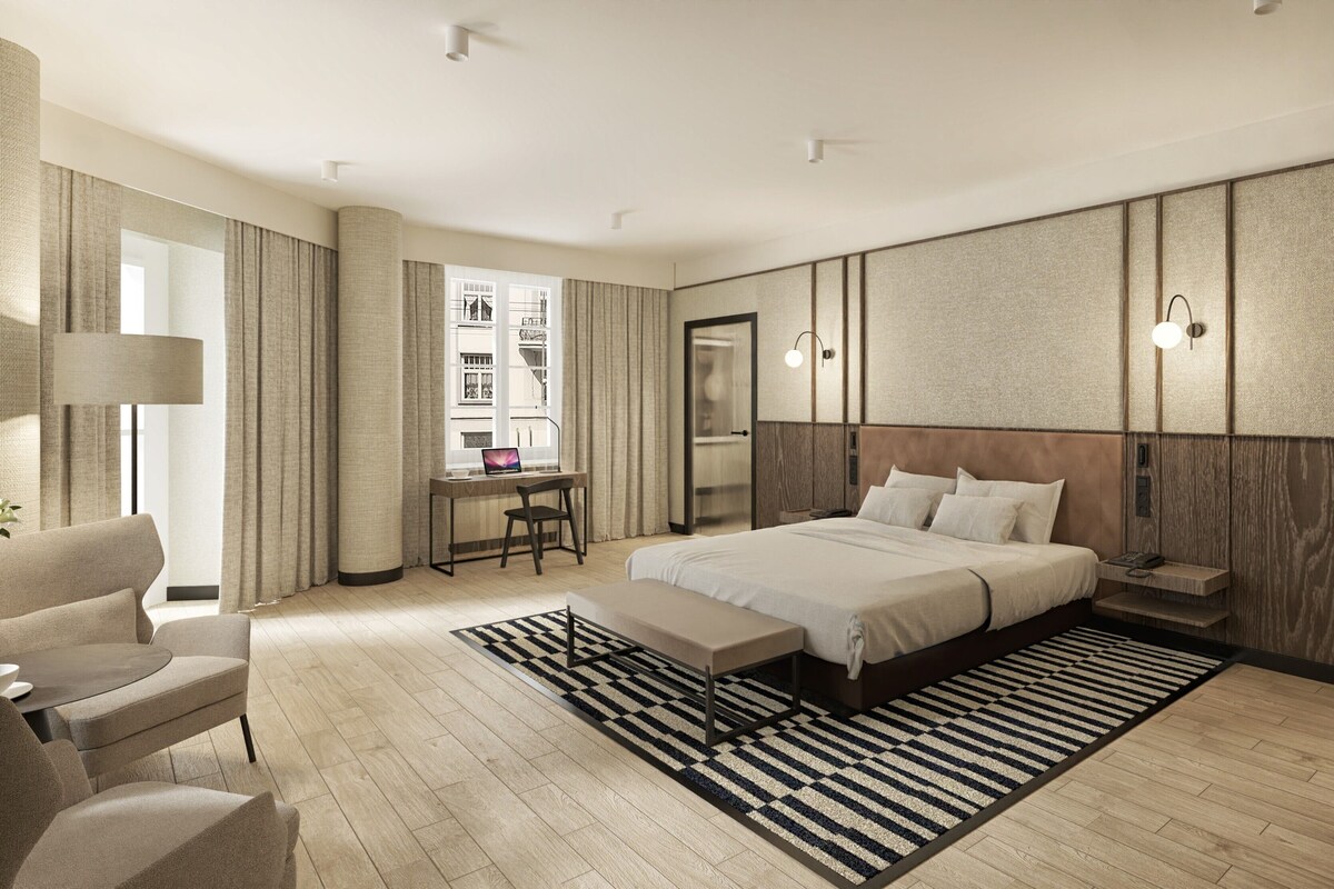 Ein modernes Hotelzimmer mit einem großen Bett, einem Schreibtisch, einem Stuhl und Blick auf die Stadt durch das Fenster.