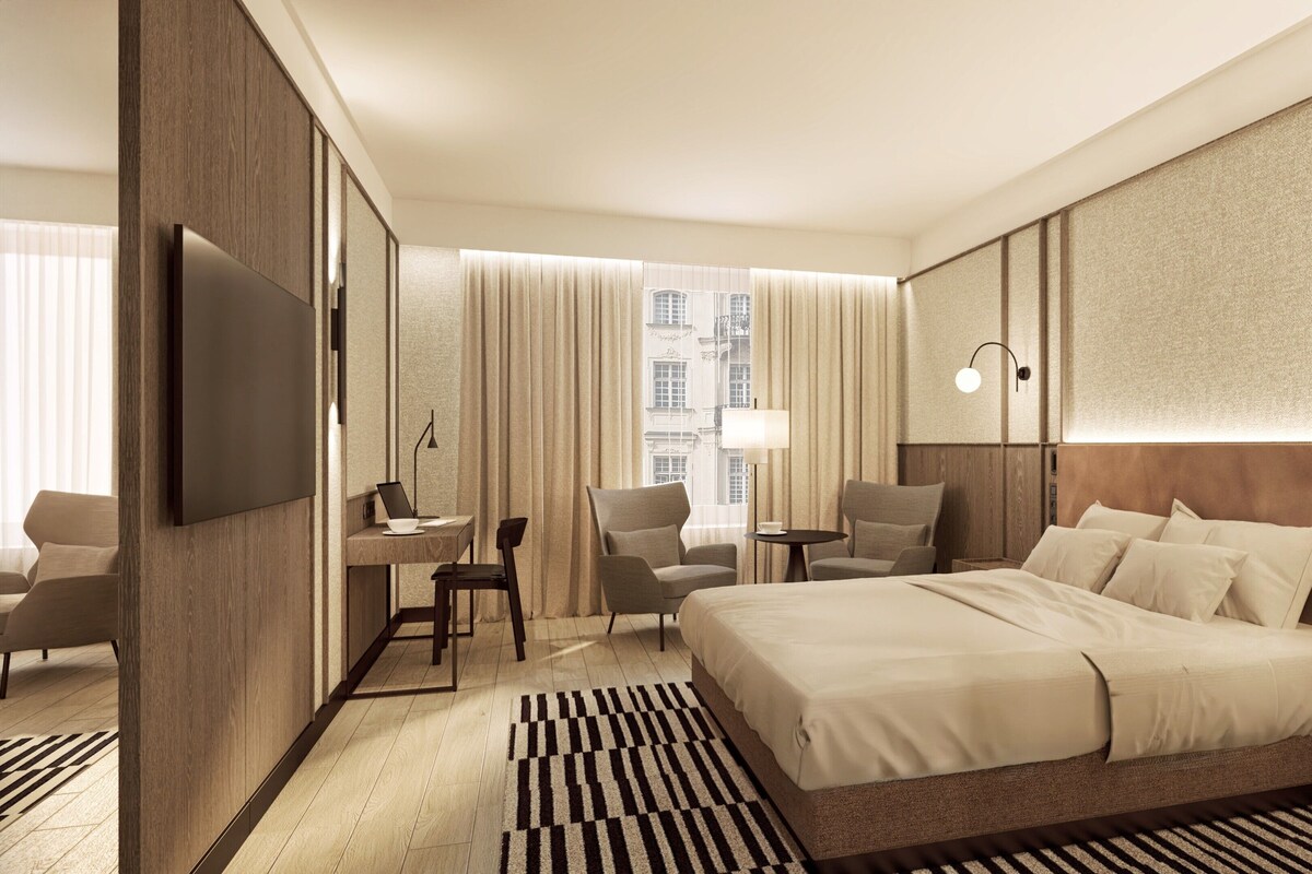 Ein Hotelzimmer mit einem großen Bett, einem Schreibtisch mit Stuhl, einem Fernseher und einem Fenster mit Vorhängen.