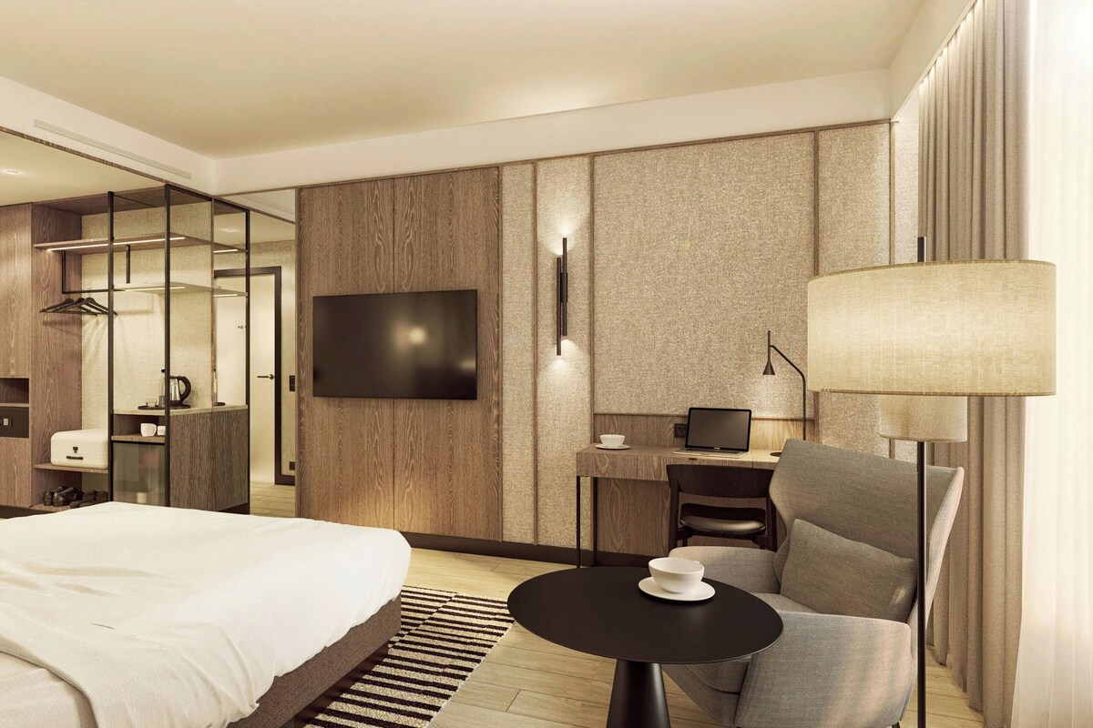 Una habitación de hotel con cama, escritorio, silla, televisor y lámpara.