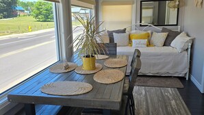 A room with a dining table set with woven placemats, a potted plant, and a sofa with cushions. - Welcome to the Lake House.  A cozy 2 Bedroom Cottage just steps from the Beach. (Central Elgin)