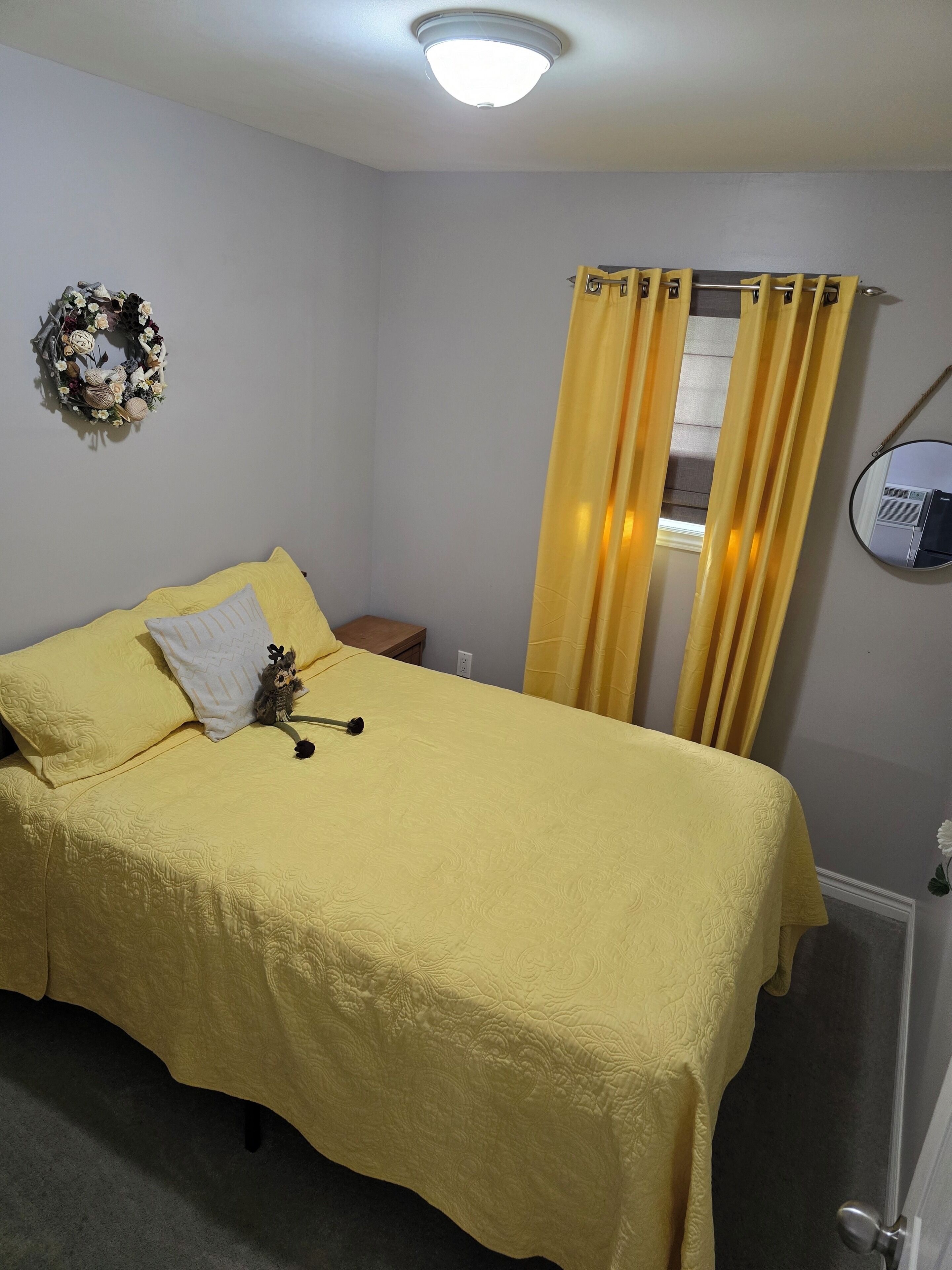 A room with a bed, a wall-mounted air conditioning unit, a curtain, and a mirror.