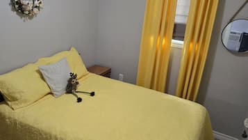A room with a bed, a wall-mounted air conditioning unit, a curtain, and a mirror.