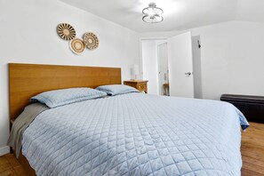 Ein Schlafzimmer mit einem hölzernen Kopfteil, einem großen Bett mit einer gesteppten blauen Bettdecke, einem Nachttisch mit Lampe und einer Tür zu einem anderen Raum.