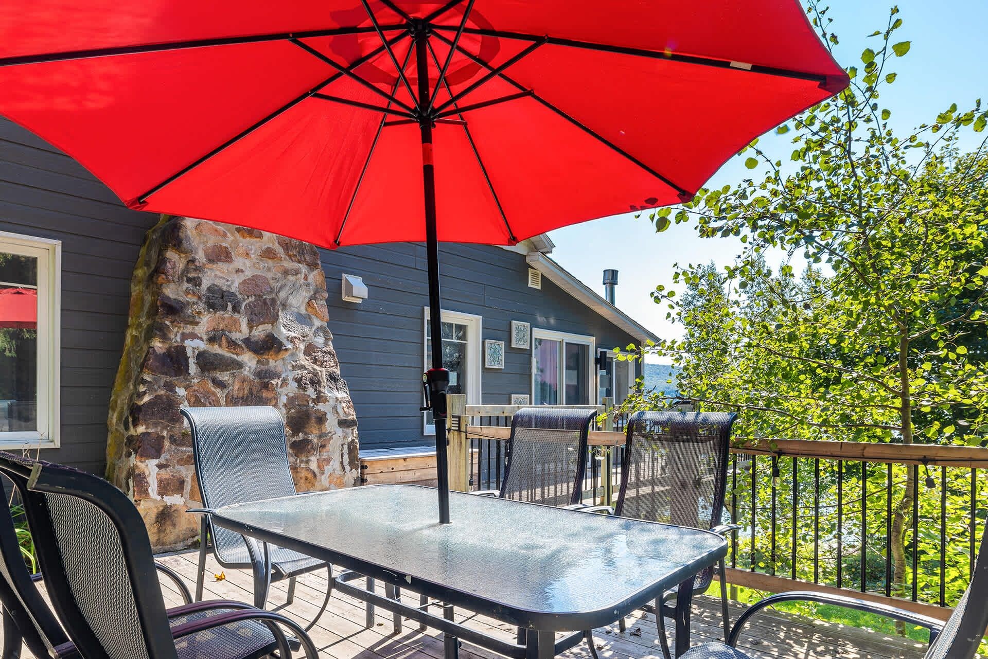 An outdoor patio with a table and chairs, a red umbrella, and a stone wall.