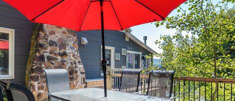 An outdoor patio with a table and chairs, a red umbrella, and a stone wall.