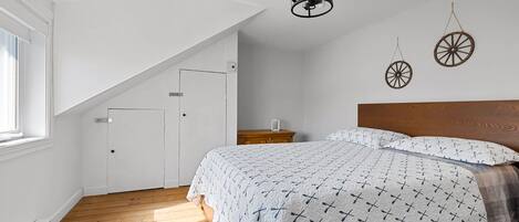 Ein Schlafzimmer mit schrägem Dach, einem hölzernen Bett, einem Nachttisch und einer Wandleuchte.