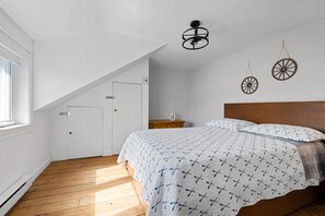 A bedroom with a sloped ceiling, a wooden bed, a bedside table, and a wall-mounted light fixture. - Clairière sur le Lac - Mandeville - Lake Waterfront (Mandeville)