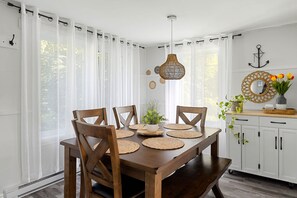 A dining area with a wooden table, chairs, and a hanging light fixture. - Clairière sur le Lac - Mandeville - Lake Waterfront (Mandeville)