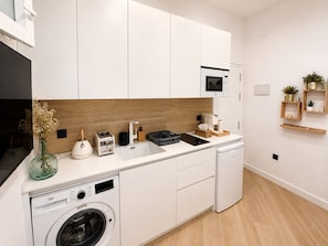 A compact kitchen with a washing machine, a sink, and a microwave. - Seville City Center | Elegant apartment for 4 people. (Sevilla)