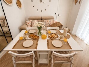 Une table à manger dressée pour le petit-déjeuner, avec des assiettes, des verres et une carafe de jus d’orange.