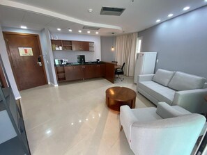 Ein modernes Wohnzimmer mit einer Couch, einem Couchtisch und einer Küchenzeile im Hintergrund.
