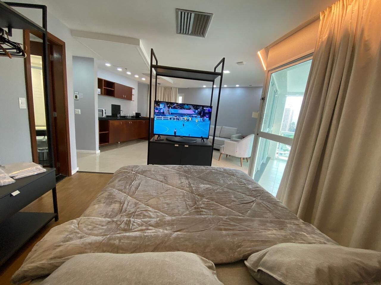 A bedroom with a bed, a TV, a wardrobe, and a view of the city.