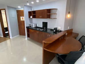 A modern kitchen with a black countertop, wooden cabinets, and a built-in microwave. - Apartment facing Barra da Tijuca beach in the former Sheraton. (Rio de Janeiro)