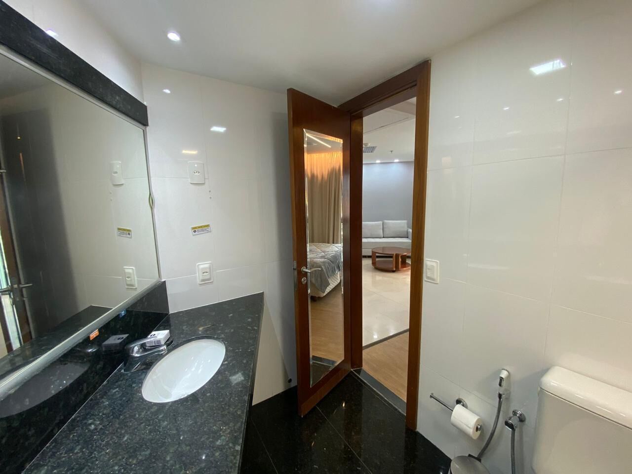 Uma casa de banho moderna com uma pia de granito preto, um espelho e uma sanita.