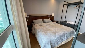 Hotellihuone, jossa on sänky, yöpöydät, riippuvalaisin ja ikkuna, jossa on verhot.
