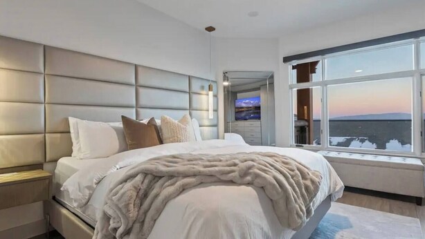 Ein modernes Schlafzimmer mit einem großen Bett, einem Kopfteil, einem Deckenventilator und Blick durch ein großes Fenster.