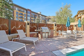 Ein Terrassenbereich im Freien mit Liegestühlen, einem Grill und einer Poolanlage.