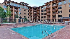 Ein mehrstöckiges Hotel mit einem zentral gelegenen Schwimmbecken, umgeben von Liegestühlen und einer eingezäunten Terrasse.