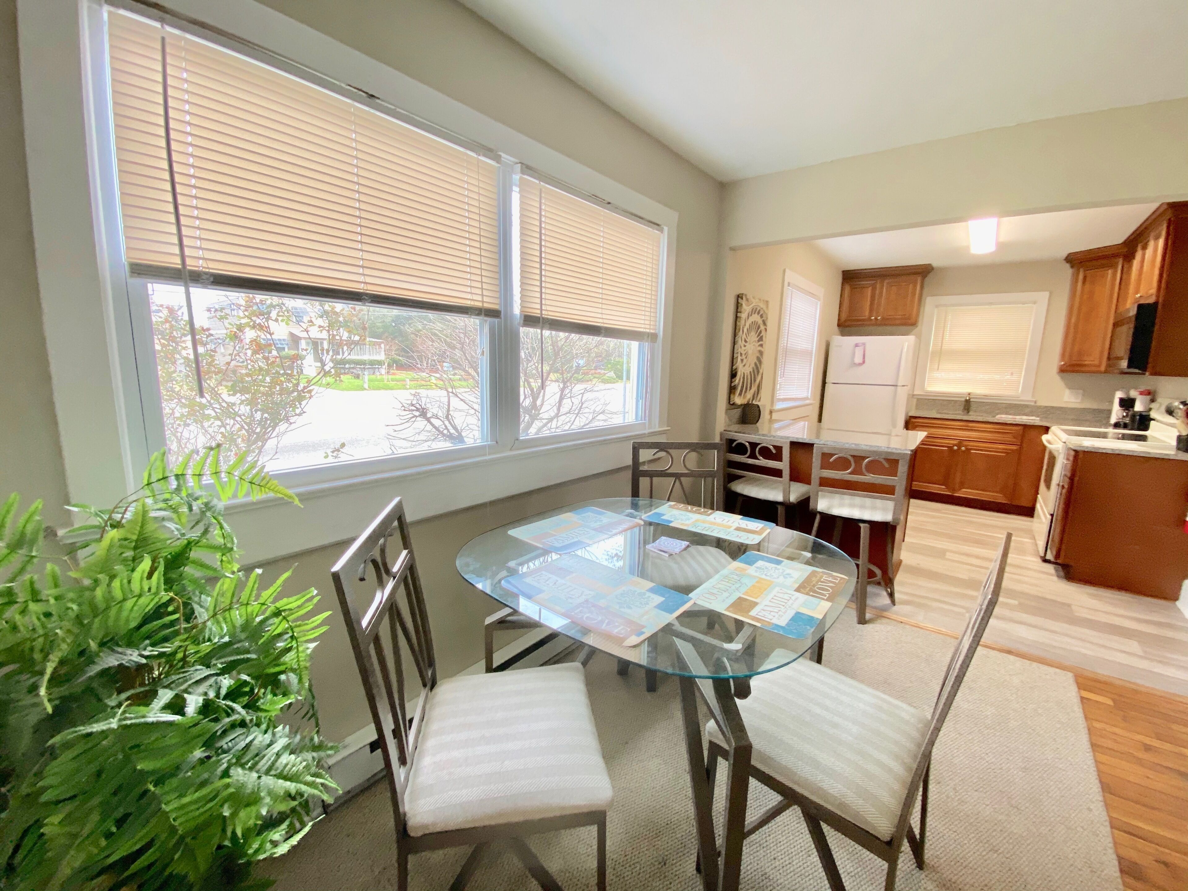 A dining area with a glass table, chairs, and a view of the outdoors through large windows.