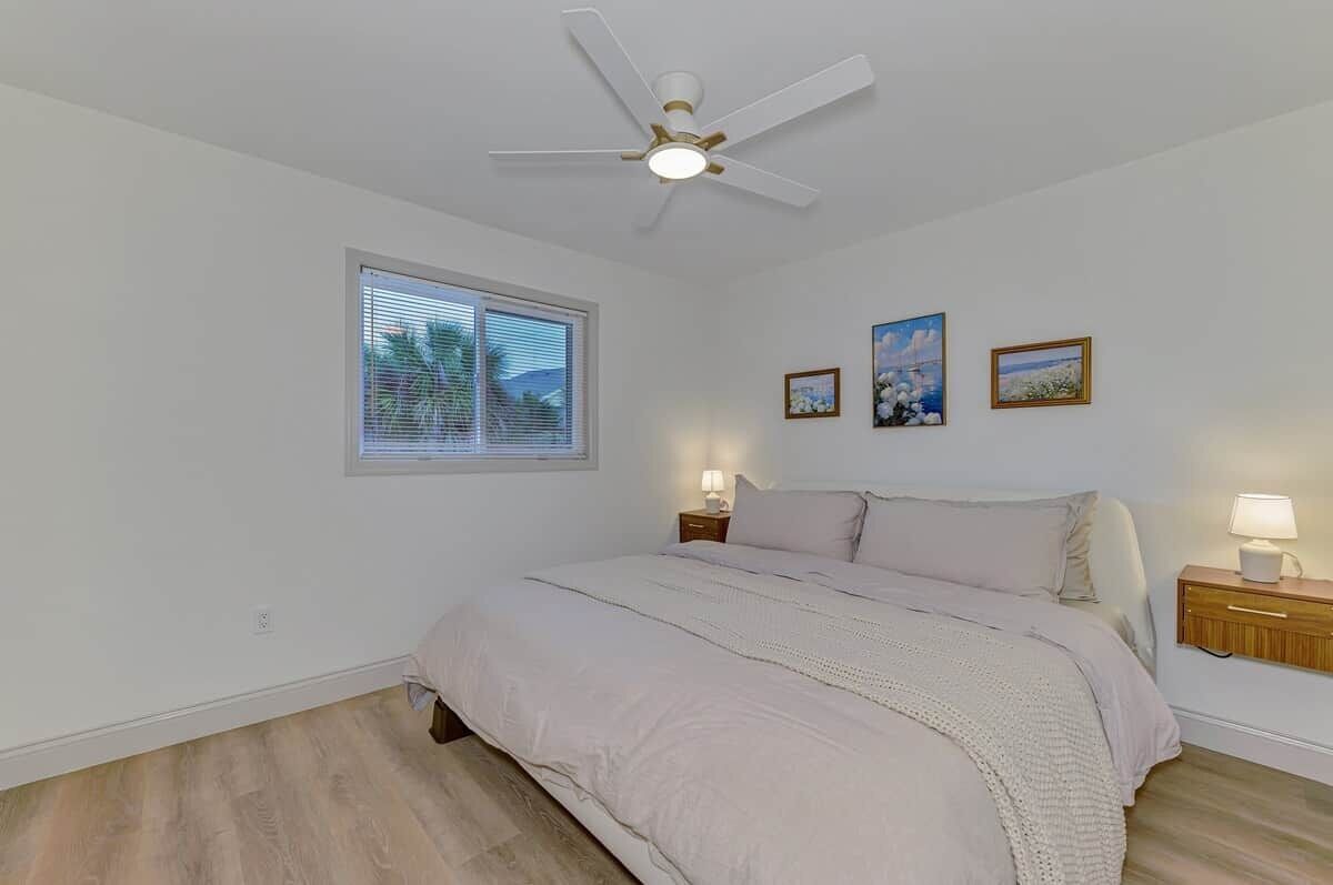 A bedroom with a bed, a ceiling fan, a window with blinds, and wall-mounted lamps.