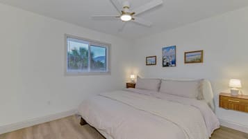 A bedroom with a bed, a ceiling fan, a window with blinds, and wall-mounted lamps.