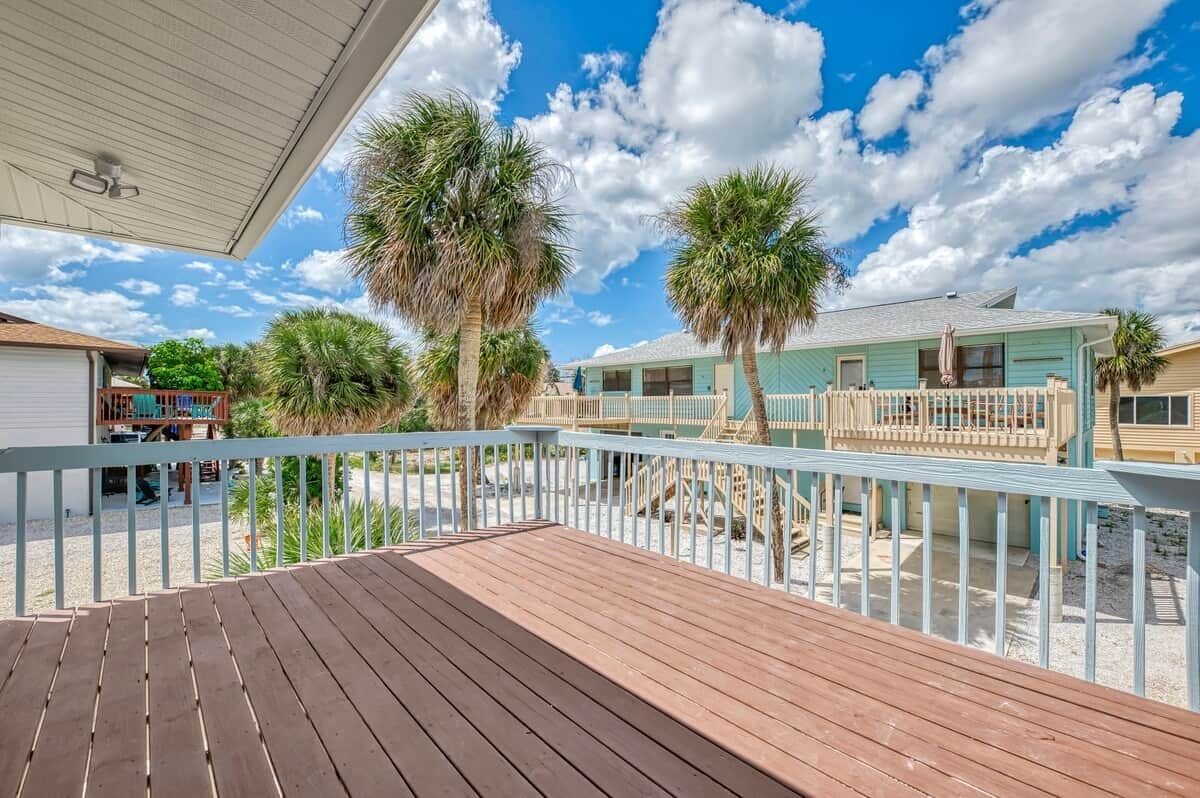 A wooden deck with a railing, palm trees, and a clear sky.
