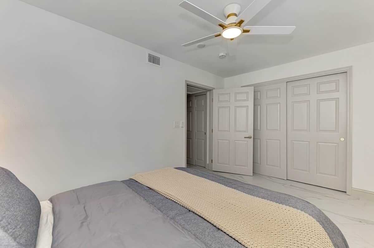 Une chambre à coucher avec un lit, un ventilateur de plafond et une porte.