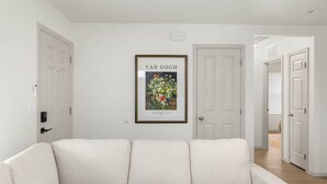 A neutral-toned living room with a framed artwork on the wall, a sofa, and a door leading to another room. - Boise Retreat, New, Hot Tub, Game Room (Ada County)