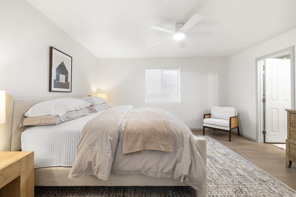 A bedroom with a bed, bedside table, chair, window, and door.