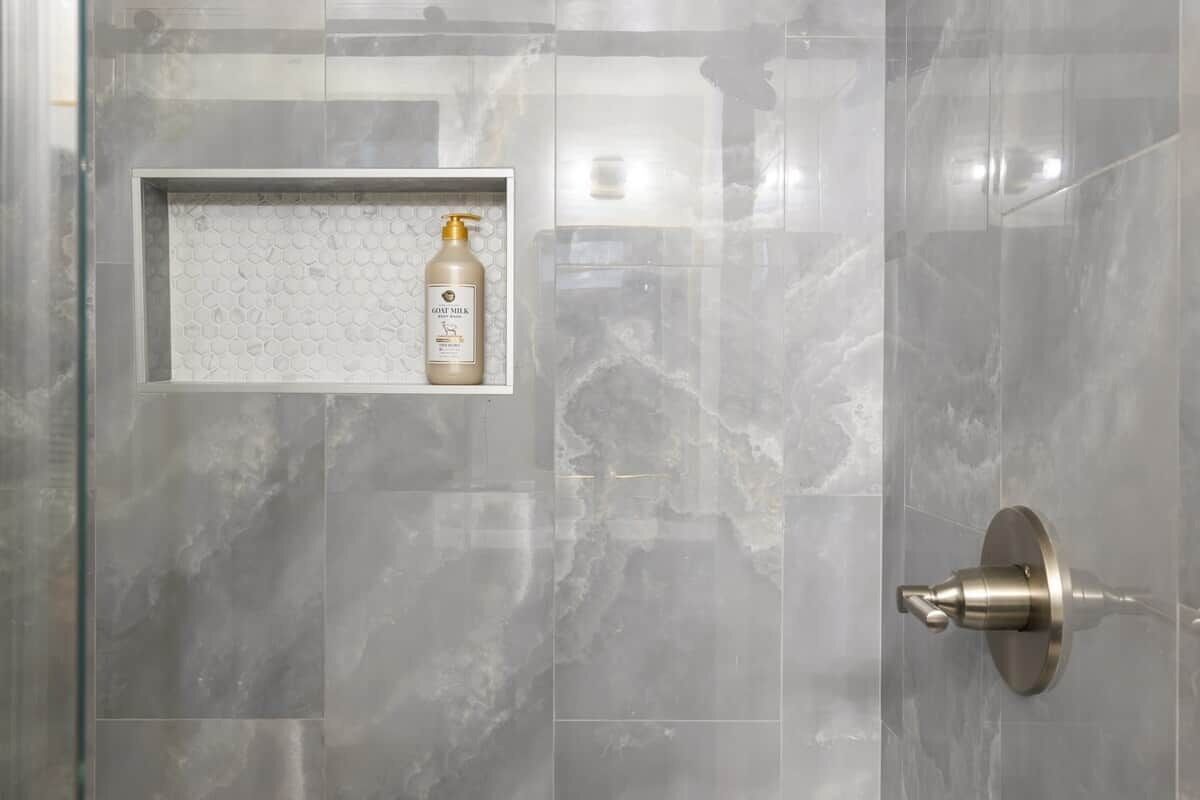 A bathroom with a shower door, a soap dispenser, and a towel rack.