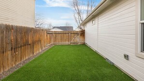 A backyard with artificial grass, a wooden fence, and a house with white siding. - Boise Retreat, New, Hot Tub, Game Room (Ada County)