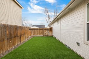 Ein Garten mit künstlichem Rasen, einem Holzzaun und einem Haus mit weißem Farbanstrich.