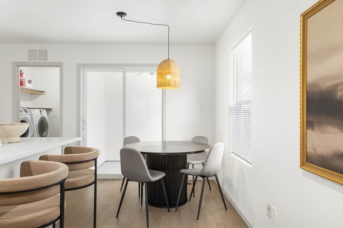 Een moderne keuken met een ronde eettafel, stoelen, een hanglamp en een groot schilderij aan de muur.