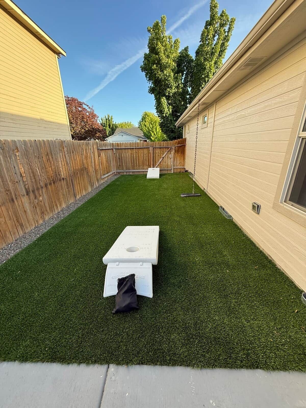 A backyard with artificial grass, a picnic table, and a wooden fence.